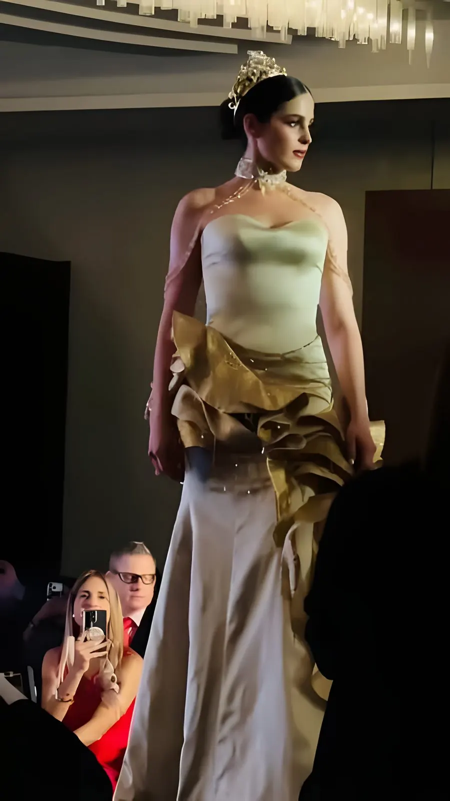 Una candidata con corona desfila con vestido marfil y dorado