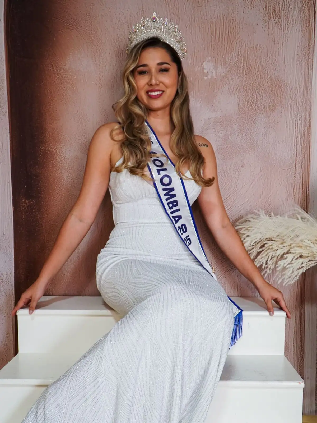 Juli, Miss Dallas Colombia 2025, sentada con vestido blanco y su corona